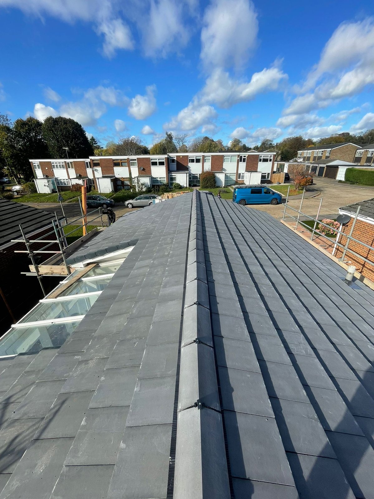 Aerial view of modern gray flat roof with solar panels on residential townhouses under blue sky with clouds